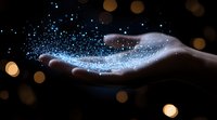 Magical glowing blue particles floating above open palm against dark background with golden bokeh lights creating mystical atmosphere.