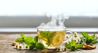 Steaming herbal tea cup with fresh mint leaves and chamomile flowers on rustic wooden table for relaxation and wellness.