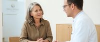 Mature woman patient consulting with male doctor in medical office discussing health concerns and treatment options during appointment.