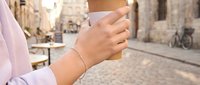 Young woman wearing delicate bracelet holding smartphone on historic cobblestone street with architecture background, urban lifestyle and technology use.