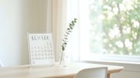 Young woman with fair skin and blonde hair sitting at wooden desk near bright window, holding eyeglasses, with eye chart and eucalyptus in vase, ideal for optometry, vision care, and wellness content.