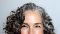 Close-up portrait of mature woman with natural gray wavy hair against light background, showcasing authentic aging and confidence for wellness and beauty campaigns.