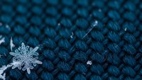 Delicate snowflake crystal resting on blue knitted wool fabric texture, winter seasonal background for cozy holiday designs and cold weather concepts.