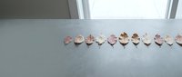 Row of pink rose quartz crystal hearts arranged on white surface near window with natural lighting for meditation and healing energy practices.
