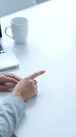 Professional hands gesturing during business meeting at white desk with coffee cup and laptop in modern office workspace for presentations.