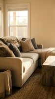 Cozy modern living room with beige sectional sofa, textured pillows and wooden coffee table in warm natural lighting for home interior design.