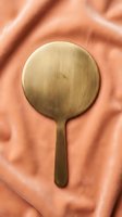 Wooden hand mirror with round reflective surface and handle resting on crumpled terracotta fabric, suitable for beauty, wellness, and lifestyle design projects.