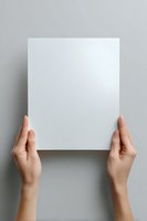 Female hands holding blank white paper sheet against gray background, mockup for presentation, branding, and design projects.