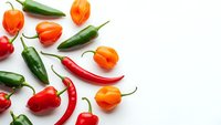 Fresh colorful hot chili peppers and physalis fruits scattered on white background. Spicy cooking ingredients for Mexican cuisine and healthy recipes.