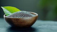 Fresh black poppy seeds in wooden bowl with green leaf on dark background, macro food photography for culinary and healthy eating concepts.