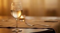 Glass of white wine on wooden table with warm golden lighting creating elegant dining atmosphere for restaurant hospitality concepts.