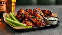 Spicy buffalo chicken wings served on black plate with fresh celery sticks and creamy ranch dipping sauce, warm ambient lighting creates appetizing mood.