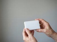 Male hands holding blank white business card against neutral gray background for corporate branding and networking purposes.