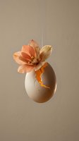 Cracked eggshell with orange flower blooming from inside, suspended by thread against neutral beige background for creative design concepts.