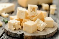 Fresh cubed Swiss cheese with distinctive holes on rustic wooden board, macro food photography perfect for culinary blogs, restaurant menus and dairy advertising.
