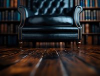 Luxurious black leather armchair against blurred library bookshelf background with vintage hardwood flooring, creating cozy reading atmosphere for interior design.