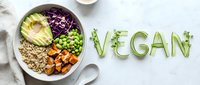 Vegan bowl with quinoa, avocado, sweet potato, edamame, and red cabbage, with the word vegan spelled in cucumber slices on marble.