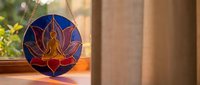 Stained glass lotus flower with meditating Buddha silhouette hanging in sunlit window, creating colorful spiritual ambiance for meditation and mindfulness practices.