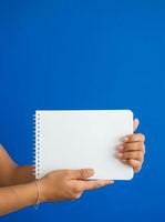 Hands holding open spiral notebook with blank pages against vibrant blue background for education, planning, and note-taking concepts.
