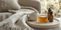 Cozy morning scene with honey and essential oil dropper bottle on concrete tray, white ceramic cup and knitted blanket against window light background.
