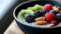 Fresh berries, kiwi, and almonds on black chia pudding in dark bowl, selective focus on mixed fruits and nuts, healthy breakfast superfood concept.