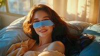 Young Asian woman wearing blue sleep mask relaxing on bed in morning sunlight, with long dark hair spread on pillow and gentle smile expressing peaceful rest.