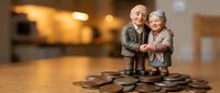 Senior couple figurines embracing on stack of coins representing retirement savings, financial planning and pension security for elderly adults.