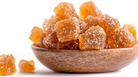 Crystallized ginger cubes coated in sugar served in wooden bowl on white background, natural healthy spicy candy and traditional medicine ingredient.