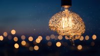 Creative brain-shaped light bulb glowing against starry night sky with bokeh lights representing innovation, ideas, creativity and inspiration.