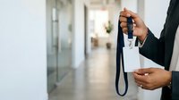 Male professional with dark skin tone holding ID badge and lanyard in modern office corridor, suitable for corporate identity, workplace security, employee onboarding, and business access themes.