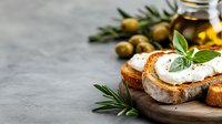 Fresh goat cheese spread on rustic bread with rosemary herbs and olives, Mediterranean appetizer on wooden board for healthy cooking and gourmet dining.