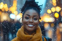 Young African American woman wearing yellow scarf smiling brightly against blurred city lights and bokeh background during winter evening, expressing joy and confidence.