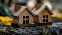 Rustic wooden miniature houses with cross-paned windows sitting on weathered wood surface against blurred natural background, creating cozy home atmosphere.