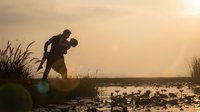 Hunter silhouette with rifle at sunset near wetland with ducks, outdoor sporting activity during golden hour hunting season for wildlife management.