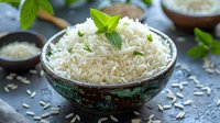 Steamed white basmati rice garnished with fresh mint leaves in rustic ceramic bowl on dark stone background with scattered grains.