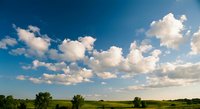 Dramatic blue sky with fluffy white clouds over green rural landscape with scattered trees on sunny day for nature backgrounds and outdoor concepts.