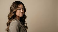 Professional Asian businesswoman with long wavy hair in beige blazer looking confident against neutral background for corporate branding and marketing.