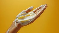 Cupped hands holding white foam or cream against vibrant yellow background for skincare and beauty product advertising concepts.