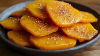 Caramelized orange slices with sugar crystals in dark bowl on wooden surface for dessert recipes and culinary presentations.