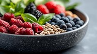 Fresh berries and lentils arranged in sections in dark stone bowl with green basil leaves, healthy breakfast ingredients on gray background, macro food photography.