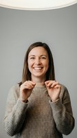 Happy young woman with long brown hair and fair complexion holding a positive pregnancy test result, wearing a beige knit sweater against neutral background for maternity, family planning and healthcare concepts.