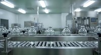 Modern pharmaceutical manufacturing facility with glass vials on stainless steel conveyor belt in sterile cleanroom environment for drug production.