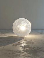 Glowing translucent sphere with textured surface resting on concrete floor against neutral wall, emitting warm light for atmospheric interior design.