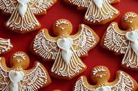 Festive gingerbread angel cookies with white icing decoration arranged on red background for Christmas holiday baking and seasonal celebrations.