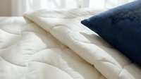 Cozy bedroom setup featuring layered bedding with white quilted comforter and navy blue pillow, ideal for home decor, interior design, and lifestyle marketing materials.