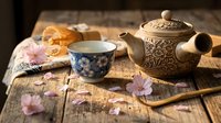 Traditional ceramic teapot and cup with floral patterns on rustic wooden table with cherry blossoms for tea ceremony and relaxation moments.