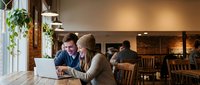 Young couple working together on laptop in cozy coffee shop cafe with warm lighting and wooden interior for business collaboration and remote work.