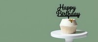 Elegant white cupcake with gold decoration and Happy Birthday topper on a white stand against a soft green background, copy space.