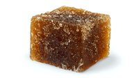 Brown sugar cube with crystallized surface texture and natural amber color on white background, isolated macro shot showing sweet ingredient detail.
