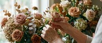 Florist arranging elegant bouquet with peach roses and eucalyptus in bright studio. Professional flower arrangement for weddings and special events.